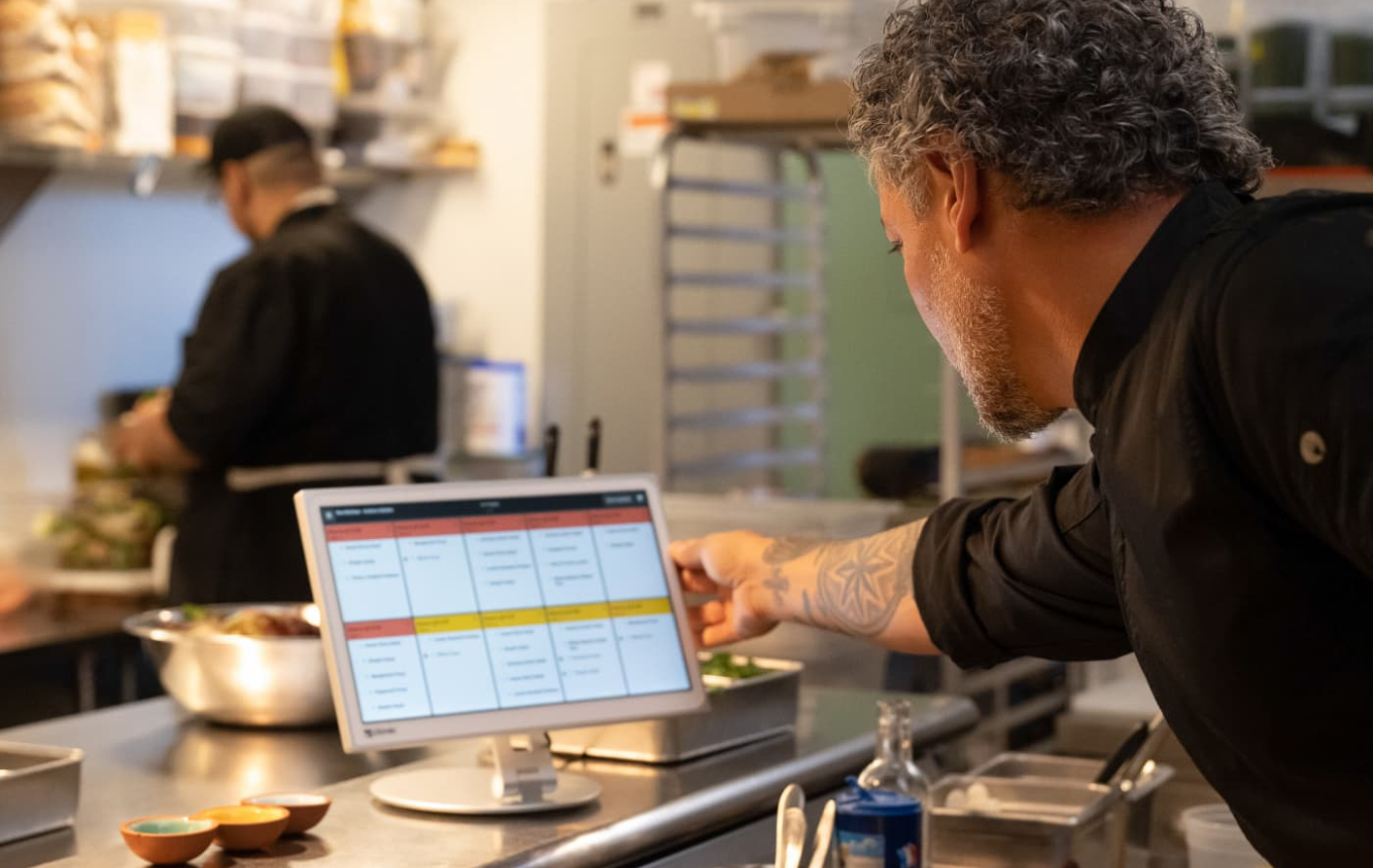 Restaurant cook plating an order next to a POS order screen